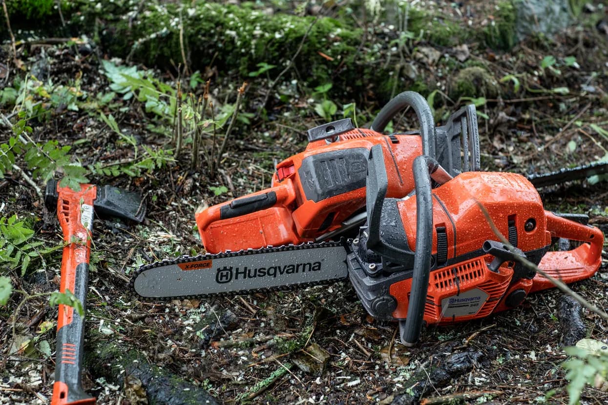 Husqvarna chainsaw and axe resting on the forest floor among wood chips